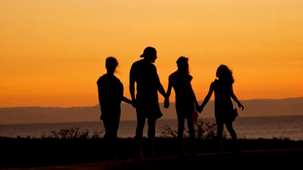 Familia tomada de la mano frente al mar al atardecer