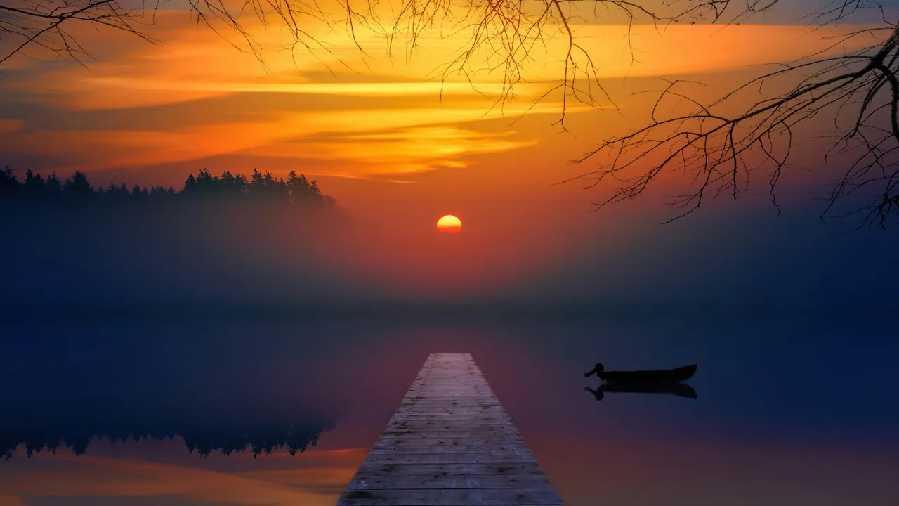 Muelle de madera que se adentra en un lago con neblina bajo un cielo anaranjado