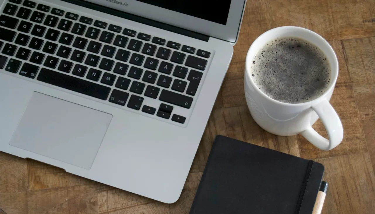 Notebook junto a una taza blanca sobre una mesa de madera